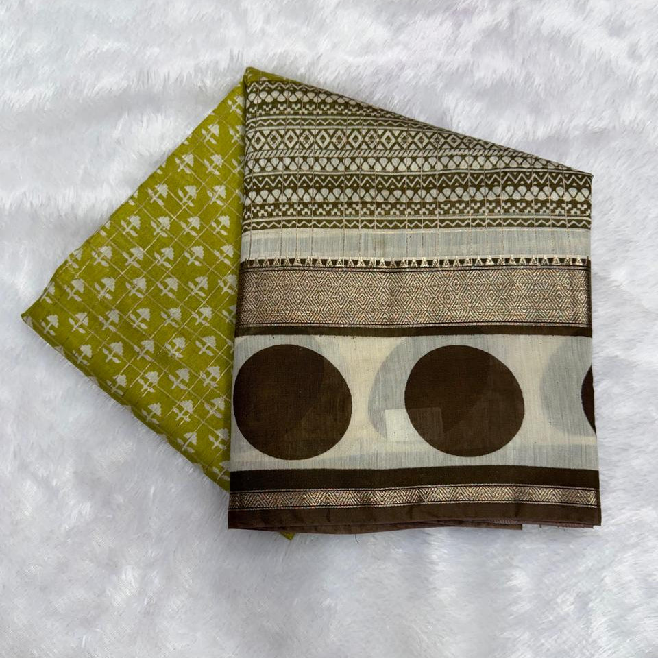 A folded piece of printed fabric laid on a white faux-fur surface, showing two patterned sides: one olive green with small white motifs and one cream and brown with geometric bands and large brown circles.